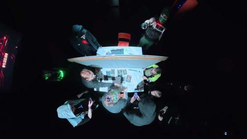 The players solving escape room-style puzzles against the clock visible in the background.