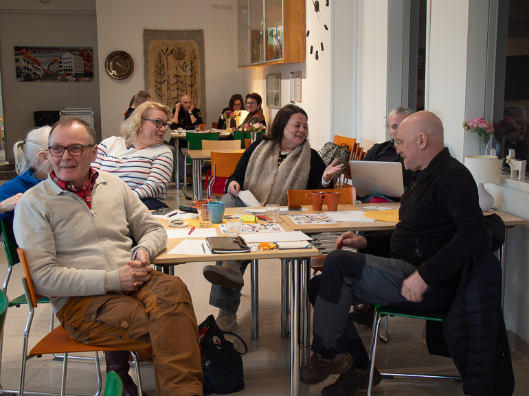 A group of 6 participants discussing around a table, another group in the background