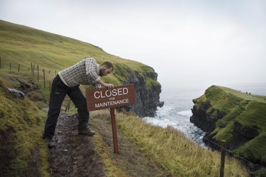 Man placing a sign on a trail that says "Closed for Maintanance"
