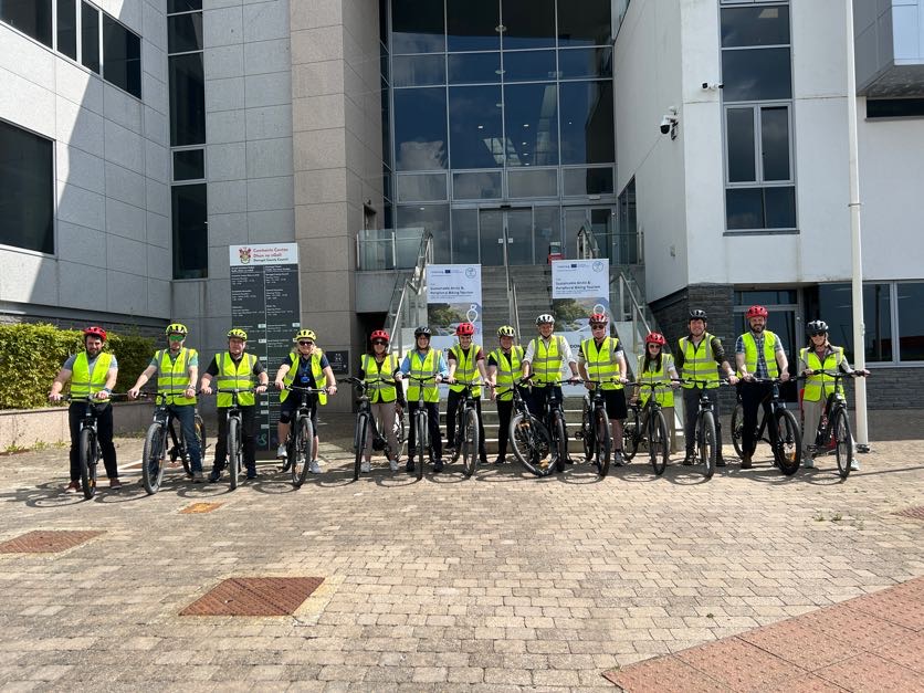 Cyclists in yellow visibility vests standing in front of a building.